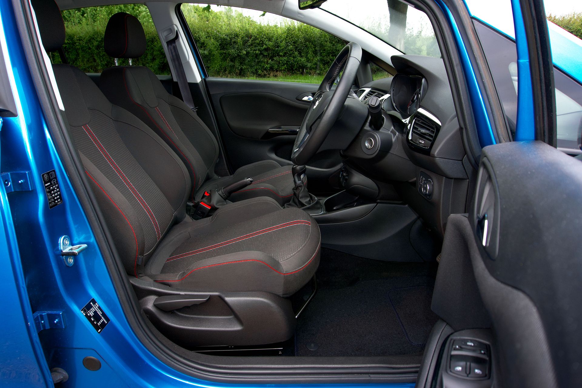 Interior of a blue car featuring black seats with red stitching and advanced dashboard design.