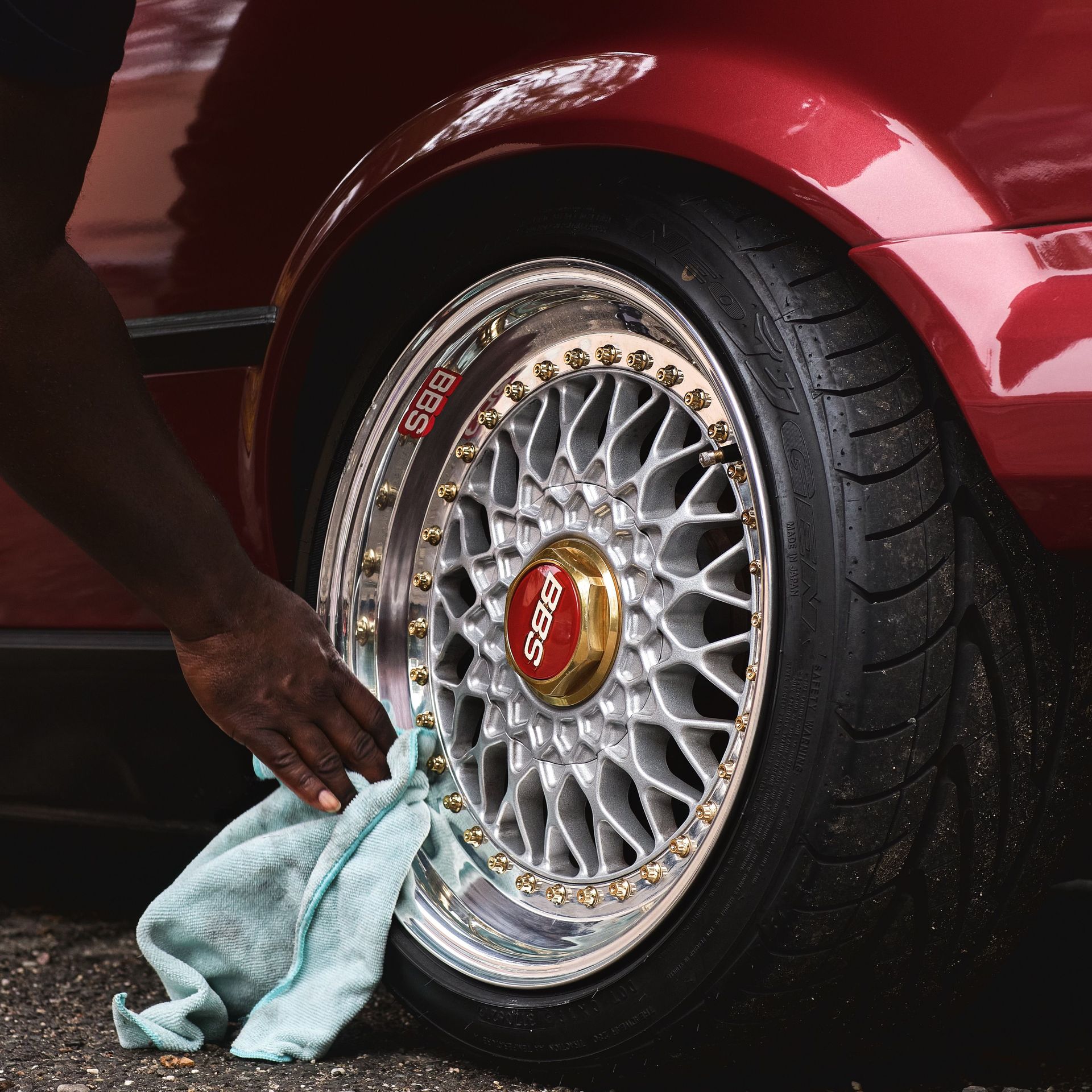 Detailed view of a person cleaning a car wheel rim with a cloth outdoors. Automotive maintenance scene.